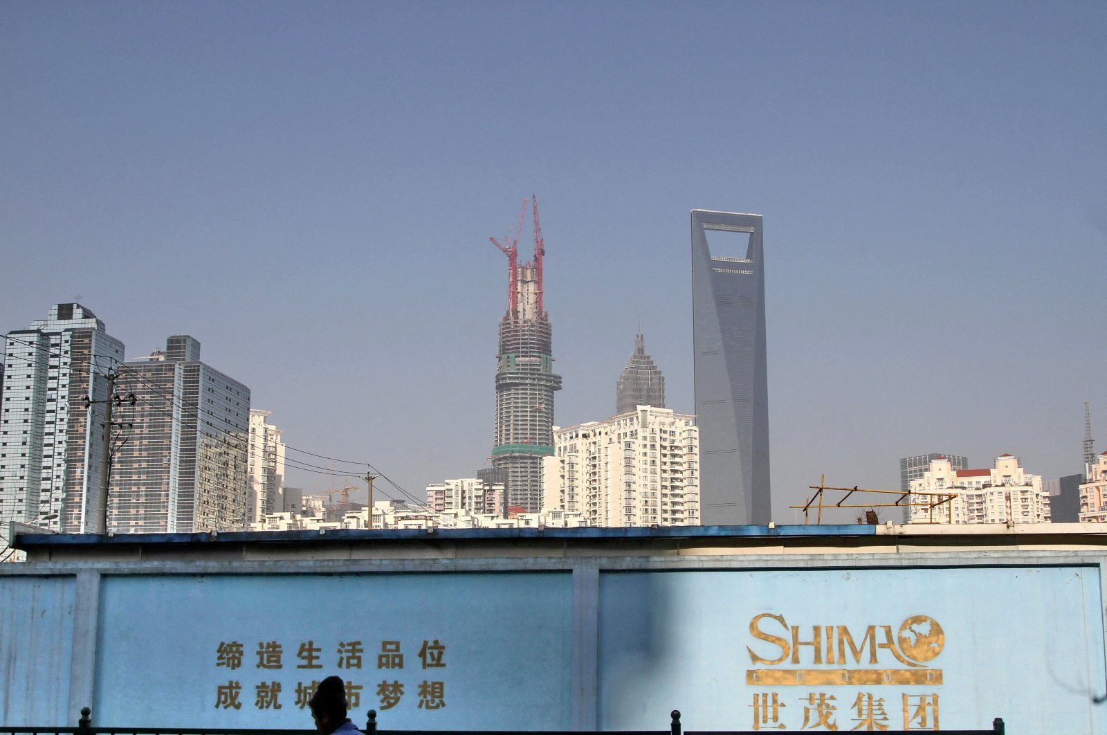 A man walks past a wall carrying the logo of Shimao Group, with residential buildings and the financial district of Pudong seen in the background in Shanghai, China, Jan. 1, 2013. (Reuters Photo)