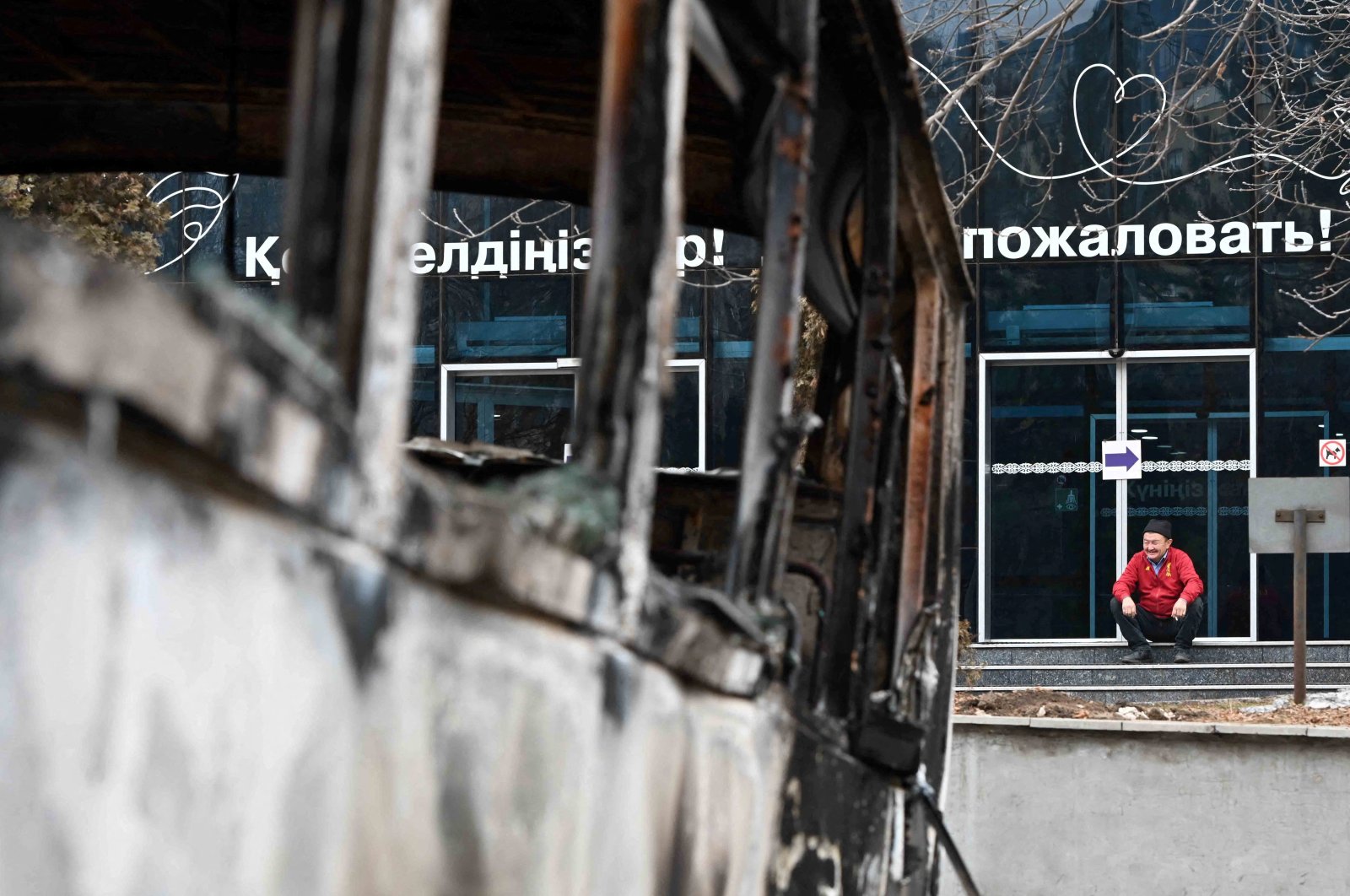 A man sits on the steps of a building as a vehicle, which was burnt during mass protests triggered by fuel price increase, is seen in the foreground, in Almaty, Kazakhstan, Jan. 9, 2022. (Reuters Photo)