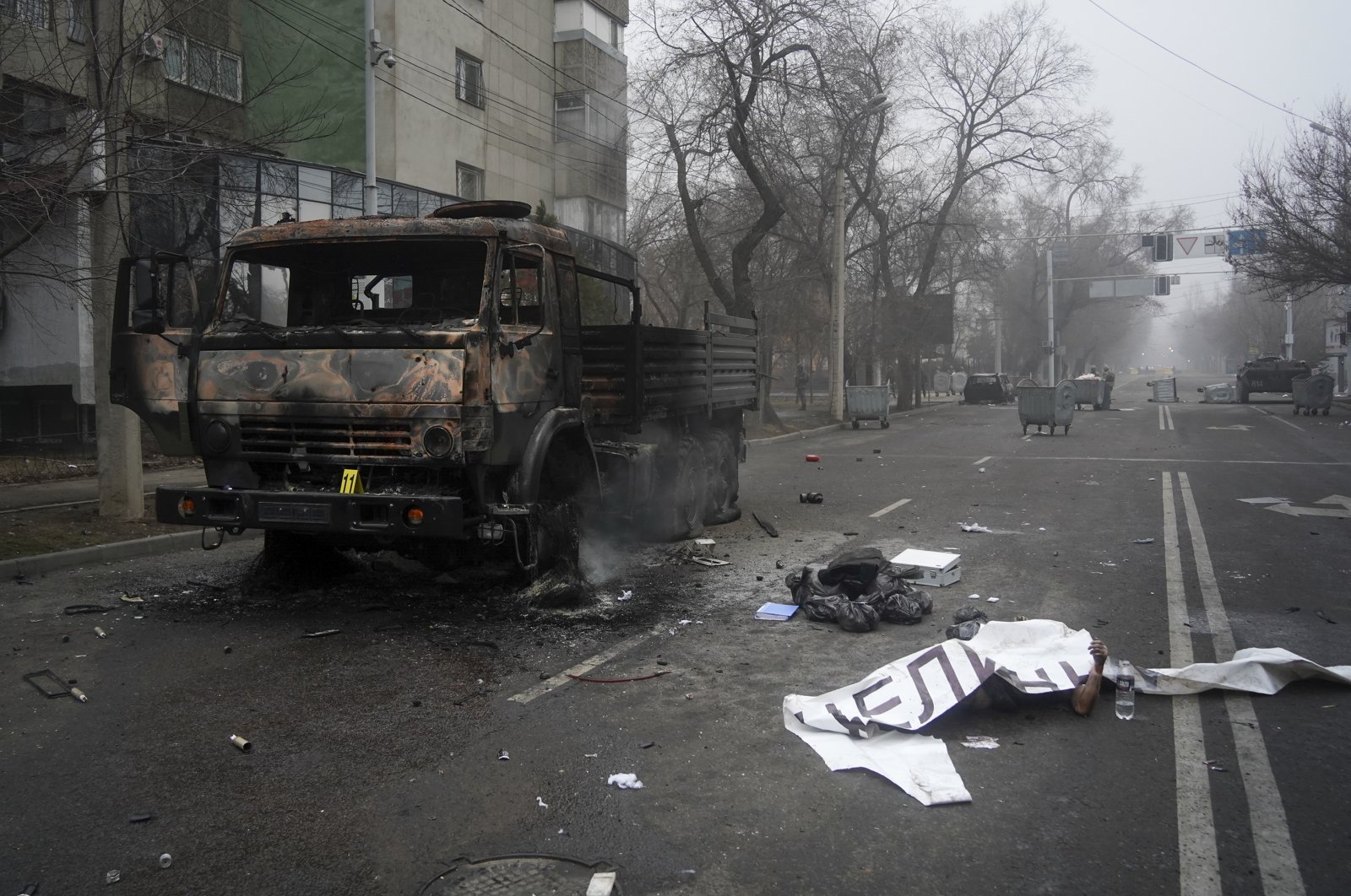 A body of a victim covered by a banner, (R), lays near a military truck, which was burned after clashes, in Almaty, Kazakhstan, Jan. 6, 2022. (AP Photo)