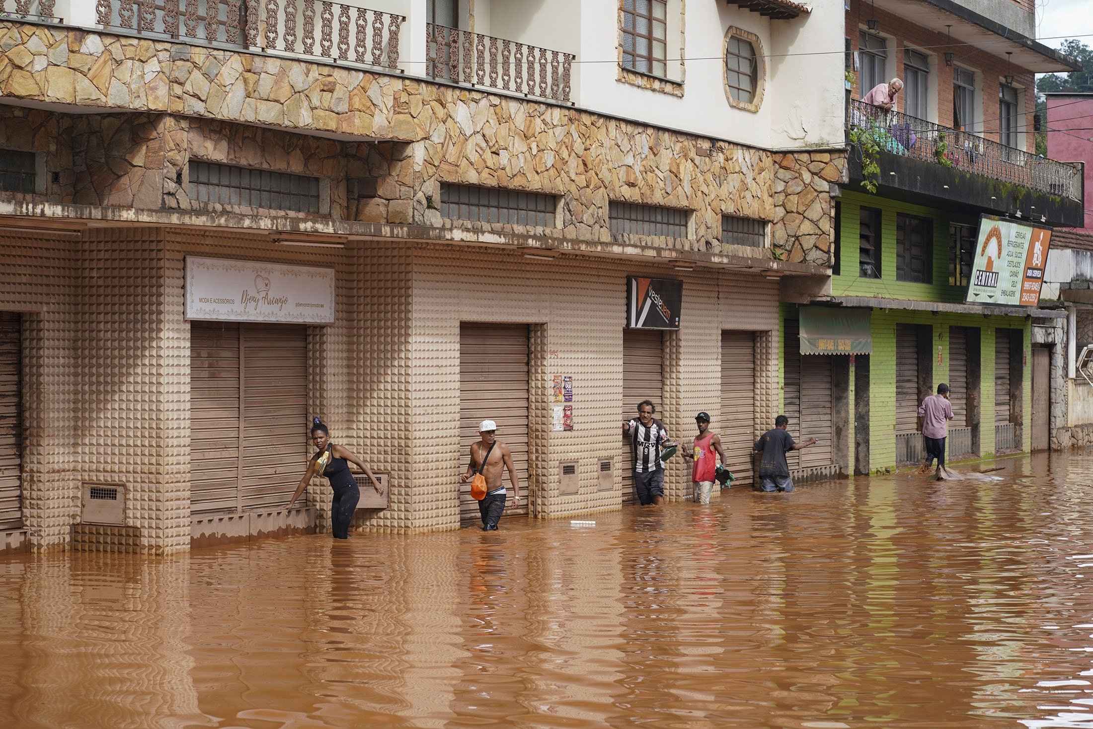 People walk in a flooded street in Raposos, Minas Gerais state, Brazil, Jan. 11, 2022. (AP Photo)