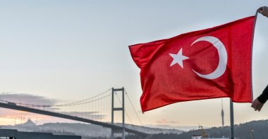 A man holds a Turkish flag in front of the 15th July Martyrs Bridge in Istanbul, Turkey. (Shutterstock Photo) 