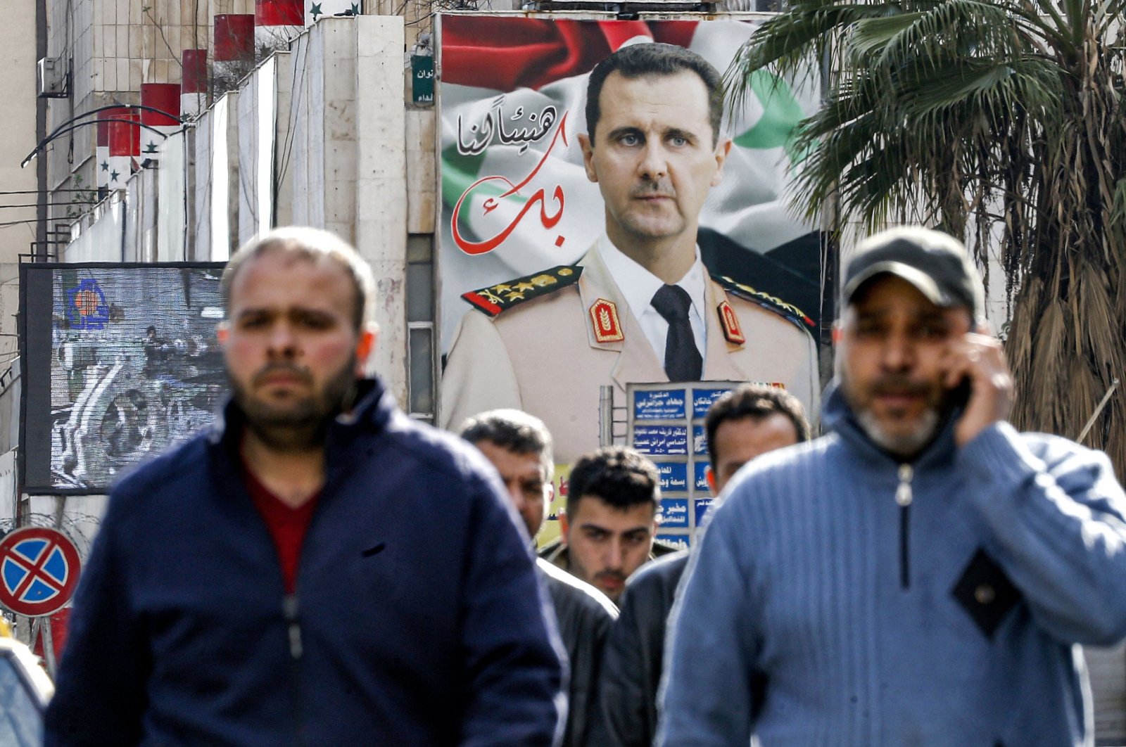 People walk past a giant billboard showing Syria&#039;s Bashar Assad dressed in military uniform along a street in the capital Damascus, Dec. 15, 2021. (AFP Photo)