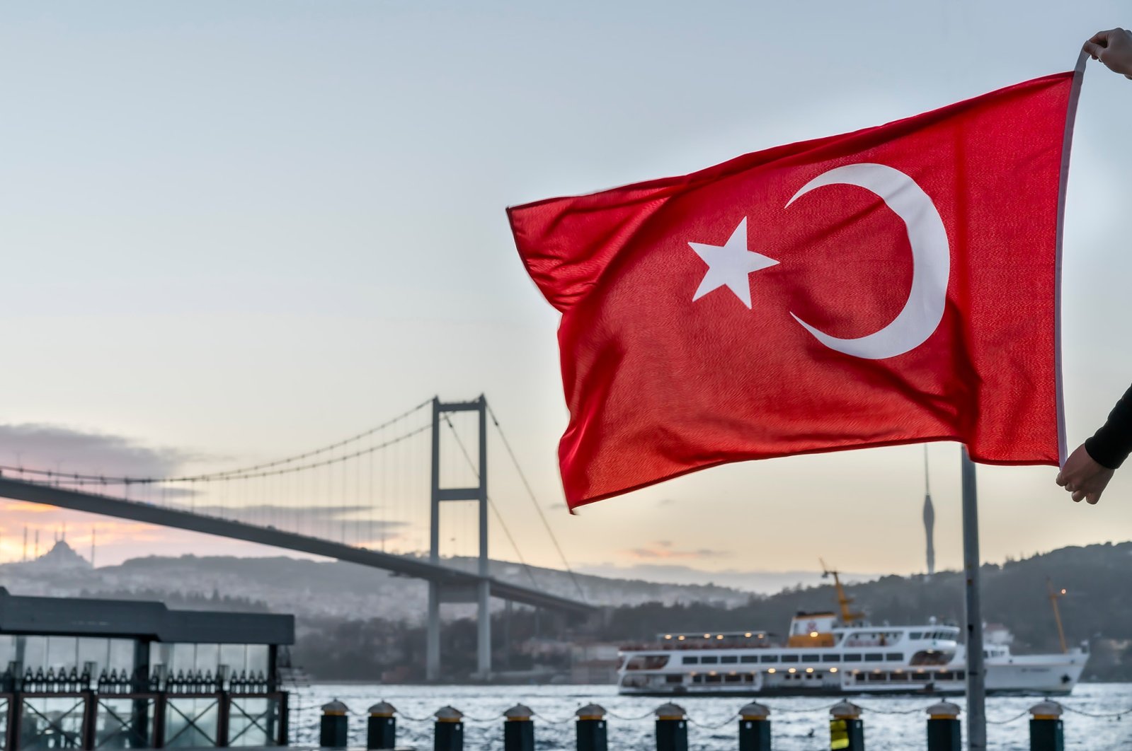 A man holds a Turkish flag in front of the 15th July Martyrs Bridge in Istanbul, Turkey. (Shutterstock Photo) 