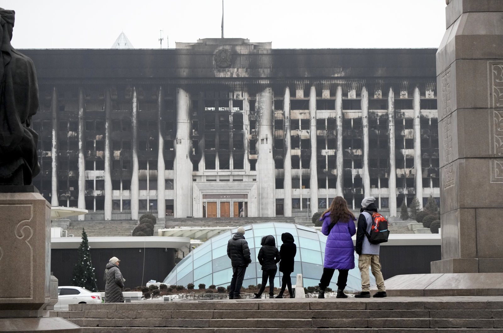 People look at the burnt city hall building in the central square blocked by Kazakh troops and police in Almaty, Kazakhstan, Jan. 11, 2022. (AP Photo)