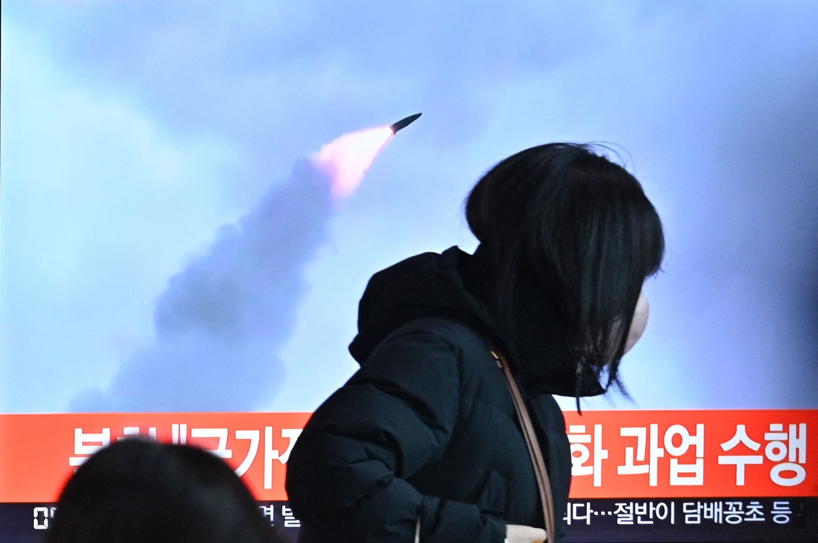 People walk past a television screen showing a news broadcast with file footage of a North Korean missile test, at a railway station in Seoul, South Korea, Jan. 11, 2022. (AFP Photo)