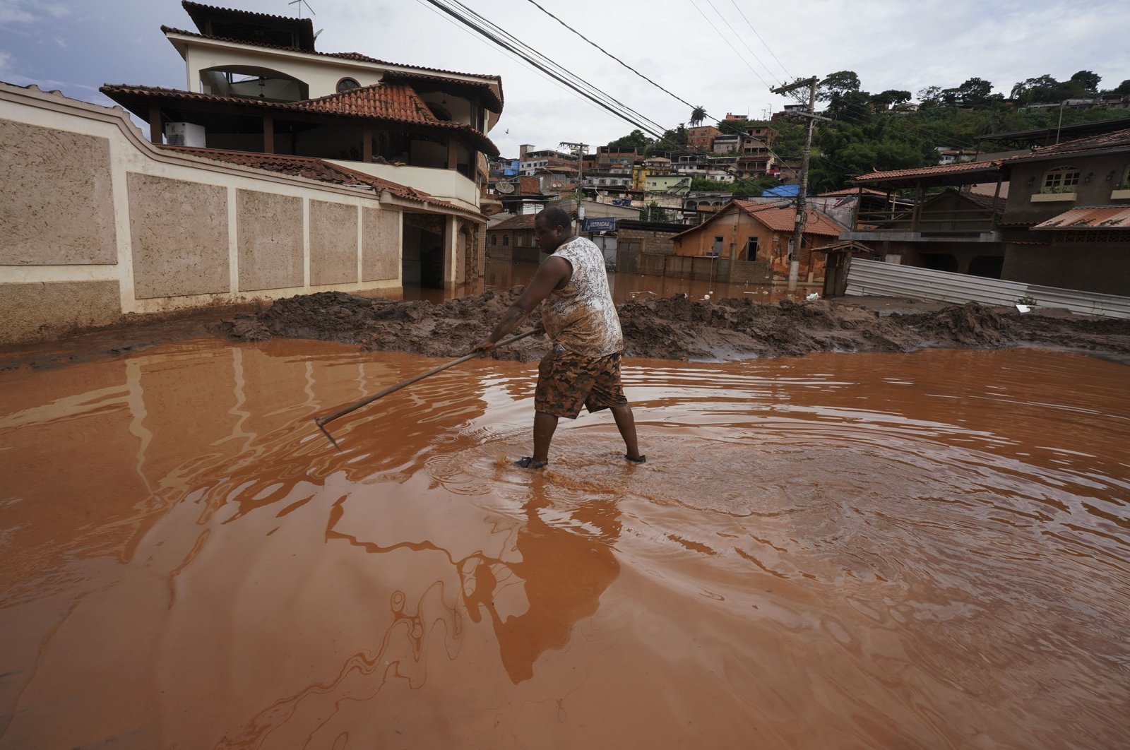 A resident removes mud from a street after flooding in Raposos, Minas Gerais state, Brazil, Jan. 11, 2022. (AP Photo)