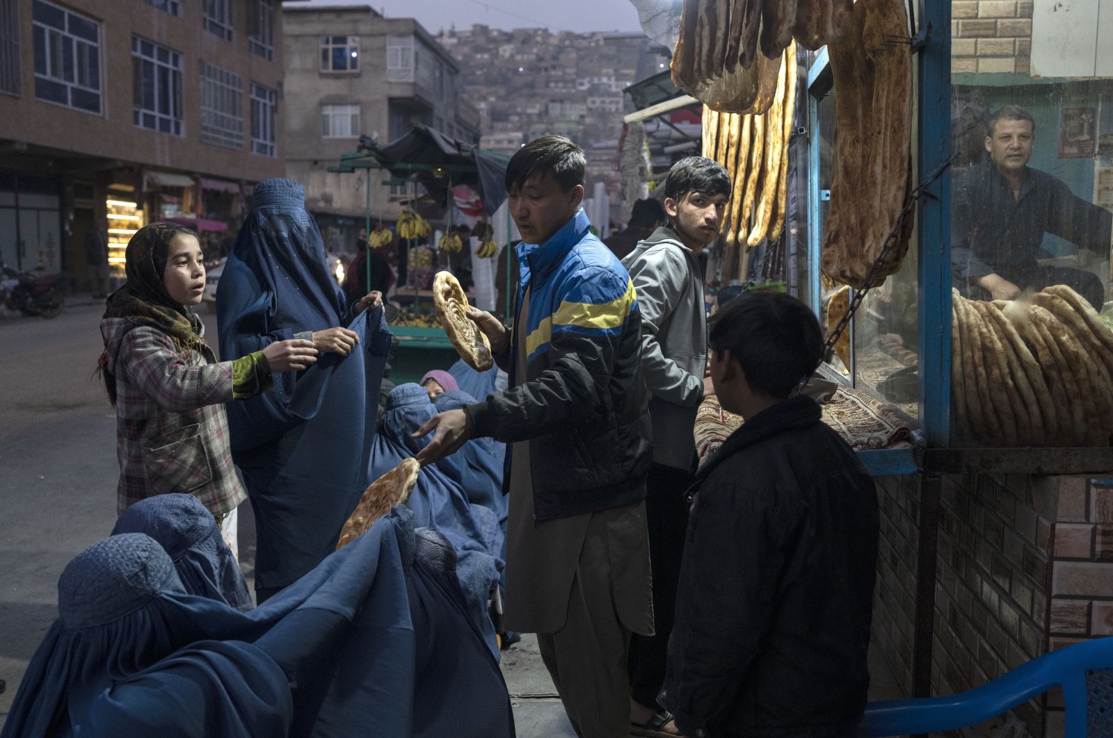 A man distributes bread to Burka-clad Afghan women outside a bakery in Kabul, Afghanistan, Dec. 2, 2021. (AP Photo)