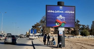 Workers sit near an electoral billboard reading in Arabic &#039;Our participation is the future of your country&#039; in Tripoli , Libya, Dec. 22, 2021. (EPA Photo)