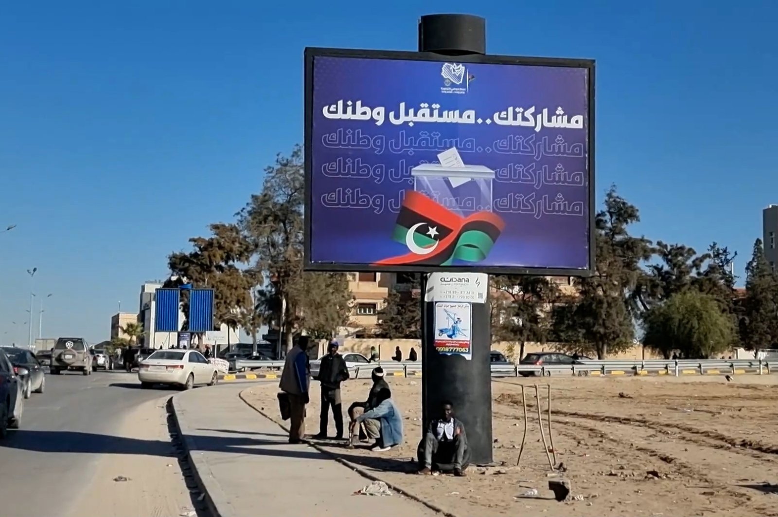 Workers sit near an electoral billboard reading in Arabic &#039;Our participation is the future of your country&#039; in Tripoli , Libya, Dec. 22, 2021. (EPA Photo)