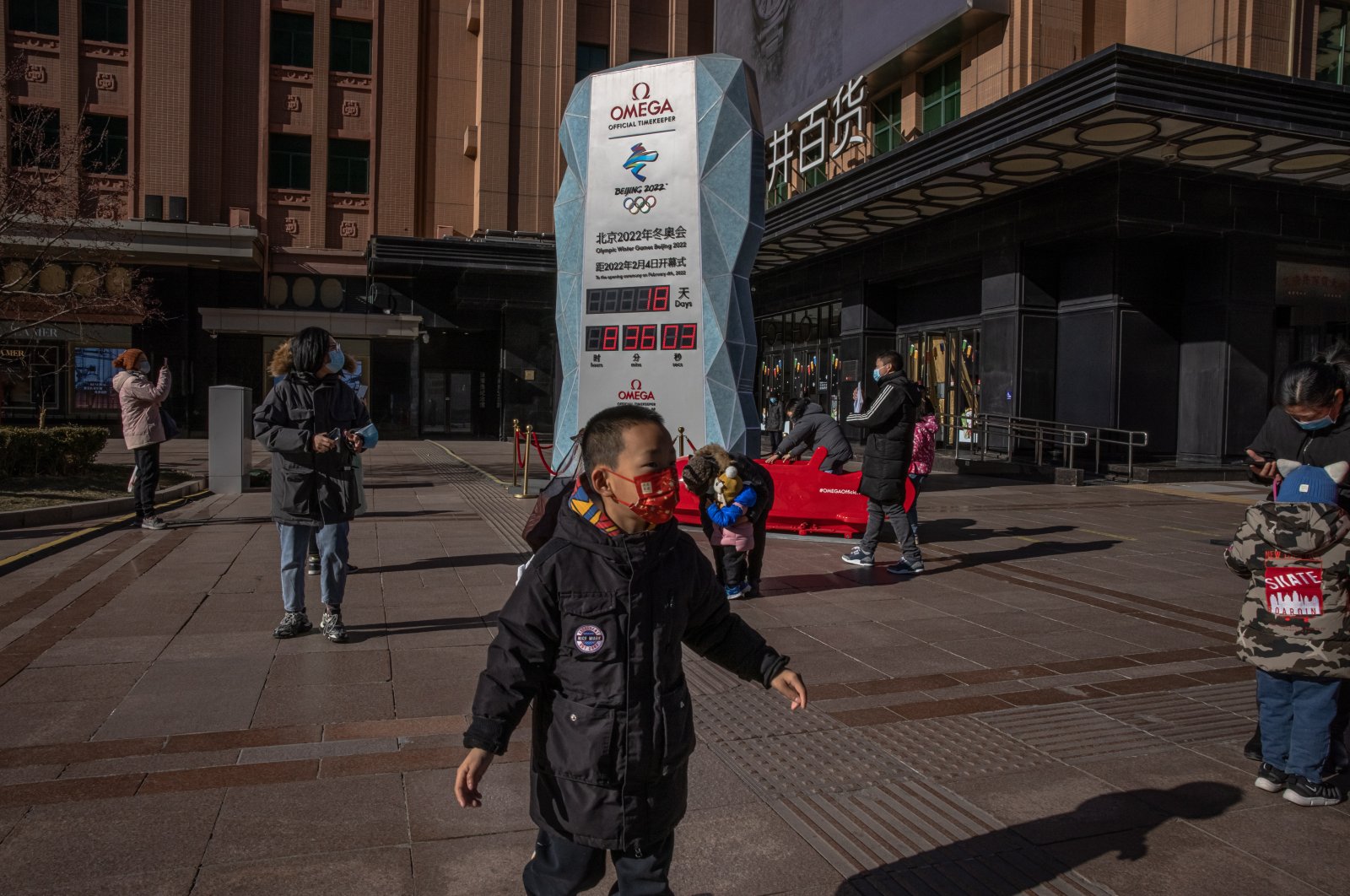 Parents with their children wearing face masks stand next to a countdown display showing days left for the Beijing 2022 Winter Olympics, on a shopping street in Beijing, China, Jan. 17, 2022. (EPA Photo)