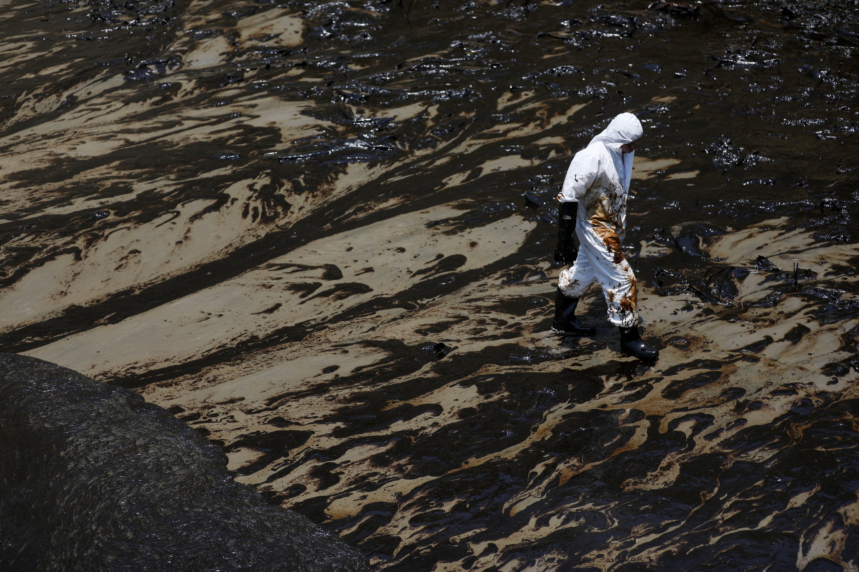 Seorang pekerja berjalan mengikuti tumpahan minyak yang disebabkan oleh gelombang abnormal, yang dipicu oleh letusan gunung berapi bawah laut besar-besaran di belahan dunia lain di Tonga, di pantai Peru di Ventanilla, Peru, 18 Januari 2022. (Foto Reuters)