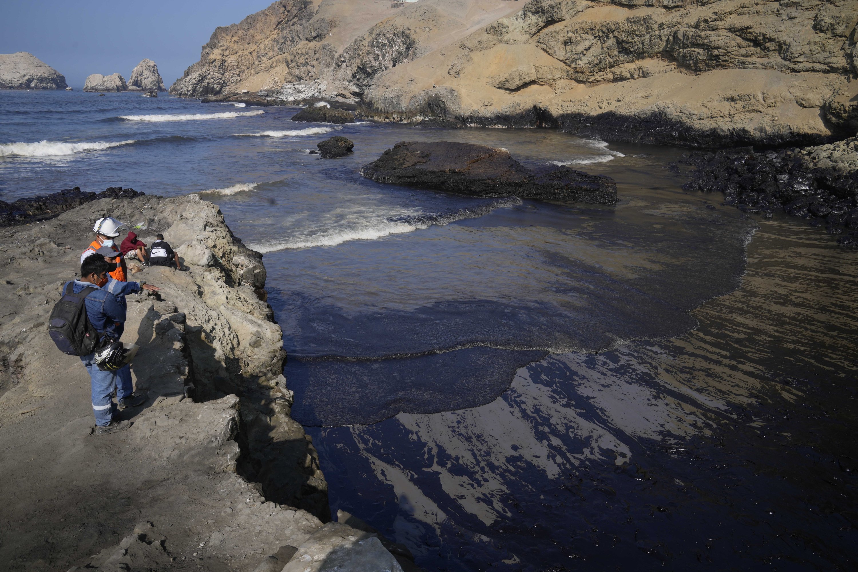 Pekerja melihat minyak di perairan Pantai Cavero setelah gelombang tinggi yang disebabkan oleh letusan gunung berapi bawah laut di Tonga menyebabkan tumpahan minyak di Ventanilla, Callao, Peru, Selasa, 18 Januari 2022. (AP Photo)