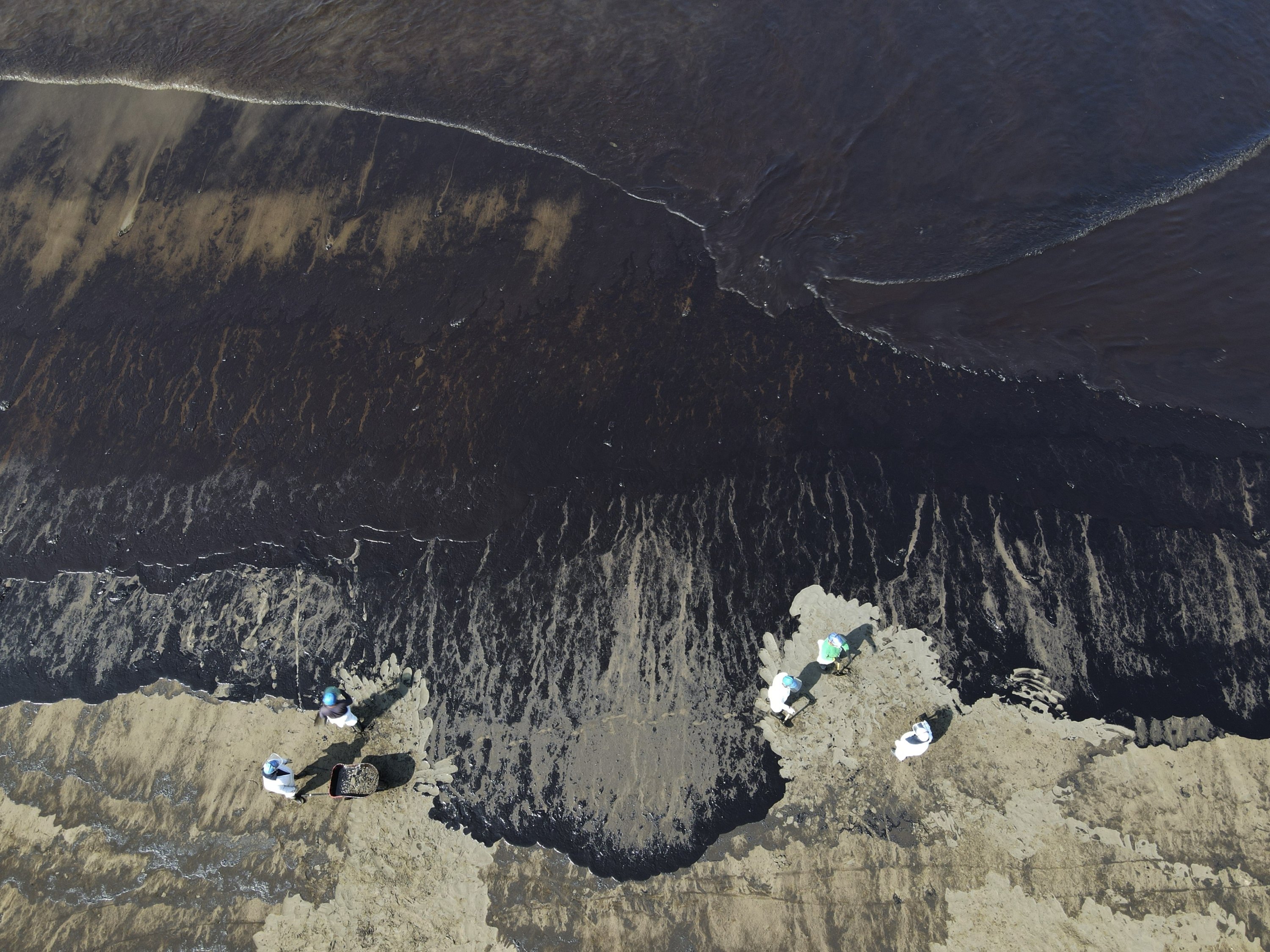 Pekerja membersihkan minyak dari pantai Cavero setelah gelombang tinggi yang disebabkan oleh letusan gunung berapi bawah laut di Tonga menyebabkan tumpahan minyak di Ventanilla, Callao, Peru, 18 Januari 2022. (AP Photo)