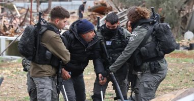 Israeli forces escort a man on crutches away from the ruins of a Palestinian house they demolished, in Sheik Jarrah neighborhood on Jan. 19, 2022. (Photo by Menahem KAHANA / AFP)