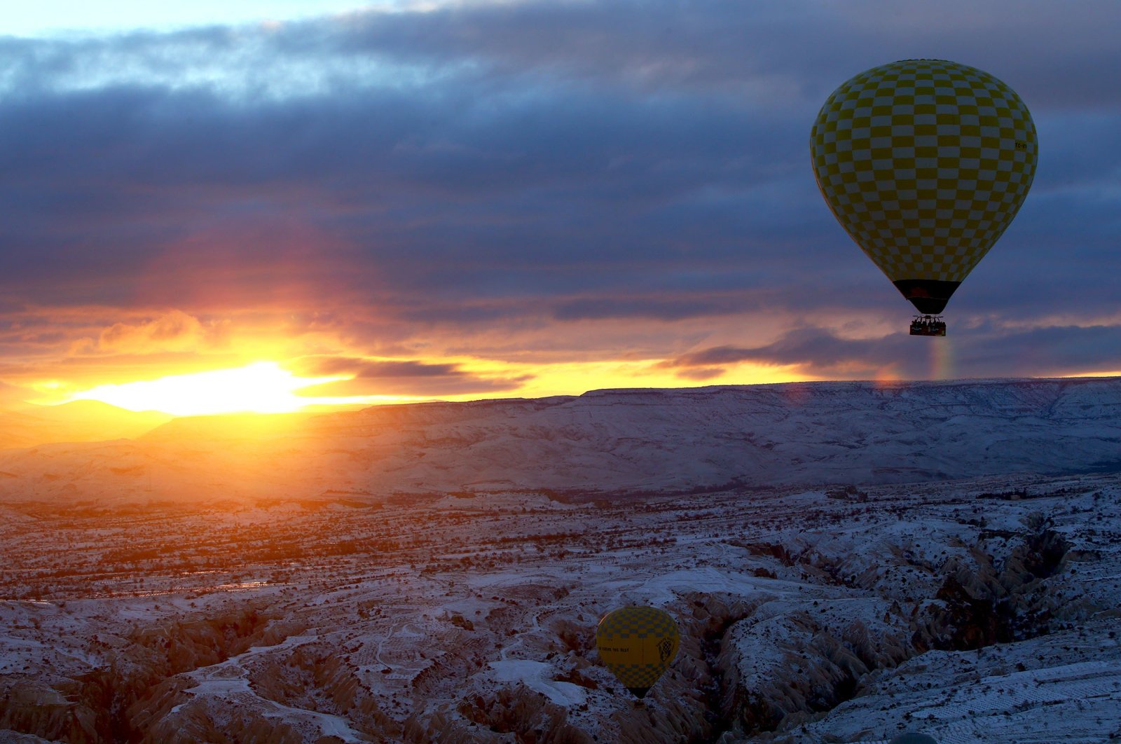 A hot air balloon soars toward the sunrise as snow blankets Nevşehir, central Turkey, Jan. 19, 2022. (AA Photo)