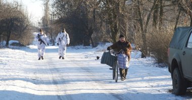 A local resident walks with his bicycle as service members of the Ukrainian armed forces are seen near the line of separation from Russian-backed rebels outside Horlivka in the Donetsk region, Ukraine, January 20, 2022. Picture taken January 20, 2022. REUTERS/Anna Kudriavtseva