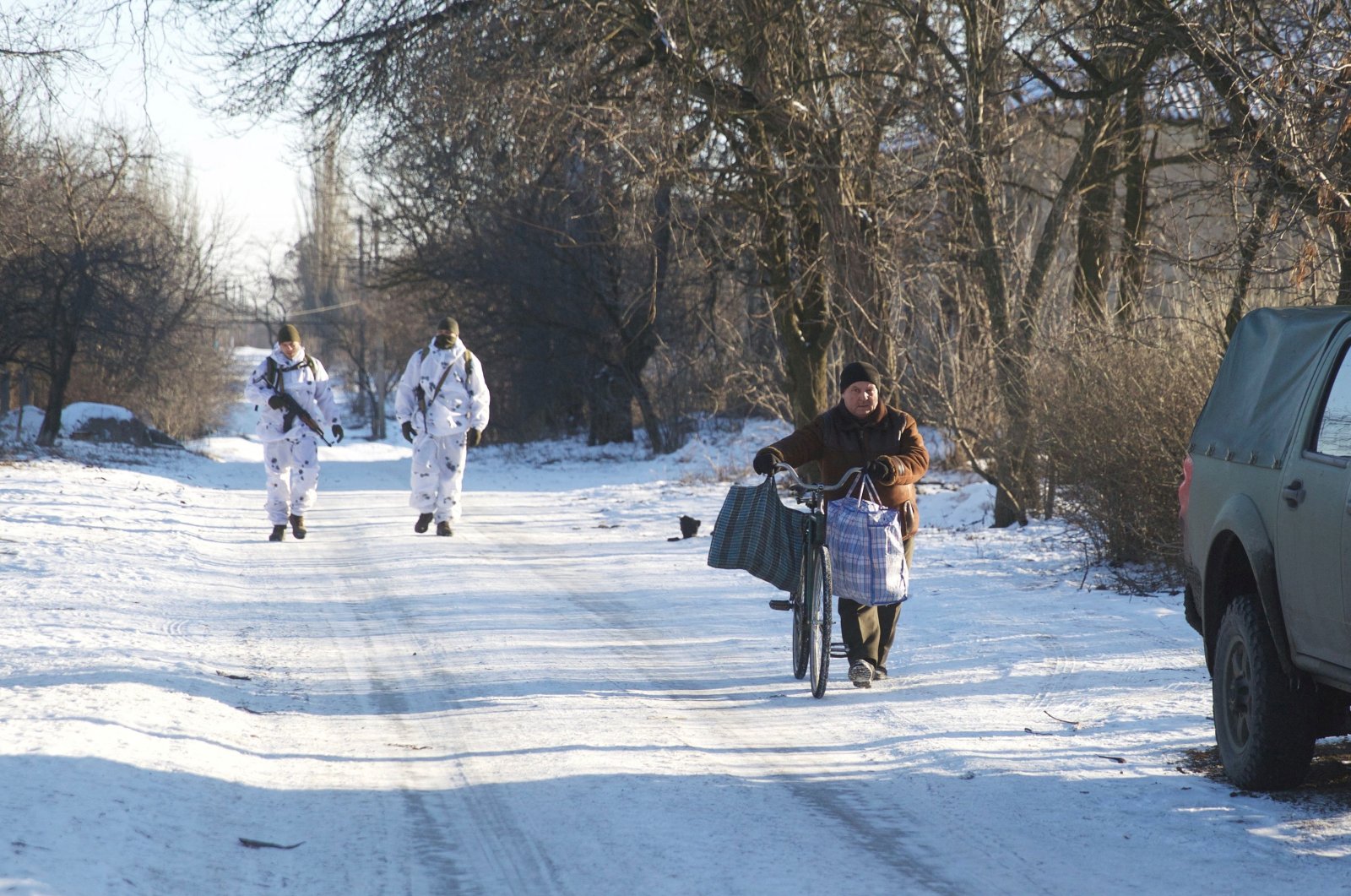 A local resident walks with his bicycle as service members of the Ukrainian armed forces are seen near the line of separation from Russian-backed rebels outside Horlivka in the Donetsk region, Ukraine, January 20, 2022. Picture taken January 20, 2022. REUTERS/Anna Kudriavtseva