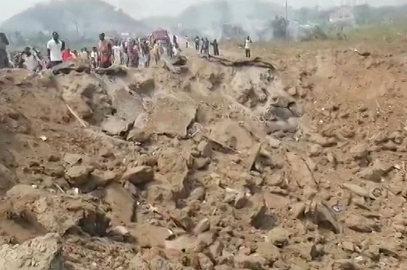 This handout video grab obtained by AFPTV from ConnectFM/TV3 on Jan. 20, 2022, shows people gathering around a large crater after a blast caused by the crash between a truck carrying explosives and a motorcycle in Apiate, near the city of Bogoso, Ghana. (Photo by Eric Yaw Adjei / ConnectFM/TV3 / AFP)