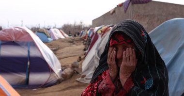 A woman at a make-shift camp for those displaced by the Taliban's regime takeover covers her eyes as the bread she bakes, fueled by plastic, produces harmful black smoke, near Herat, Afghanistan, Jan. 16, 2022. (Bilal Guler / Anadolu Agency)