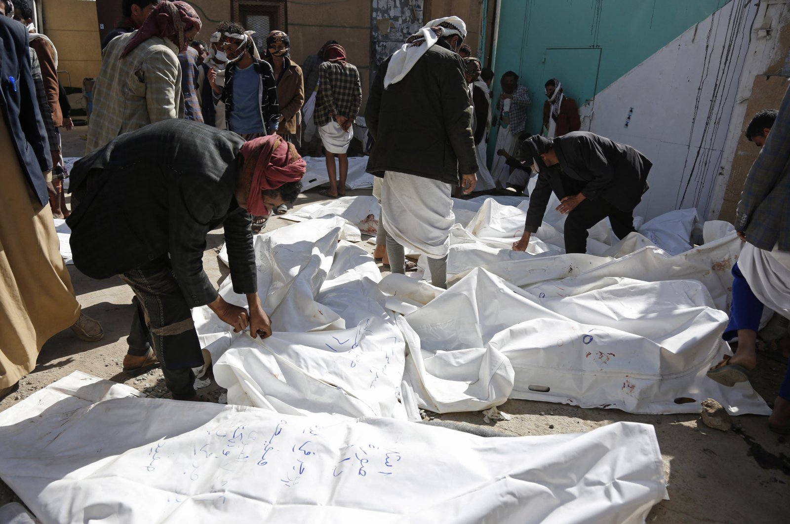 People look at the covered bodies of casualties from a Saudi-led coalition airstrike that killed at least 87 people, in a stronghold of Houthi rebels on the border with Saudi Arabia, in the northern Saada province of Yemen, Jan. 22, 2022. (AP Photo)