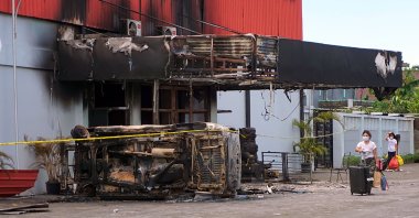 A woman carry her belonging as she walks near a torched nightclub in Sorong, West Papua province, Indonesia, Jan. 25, 2022. (AP Photo)