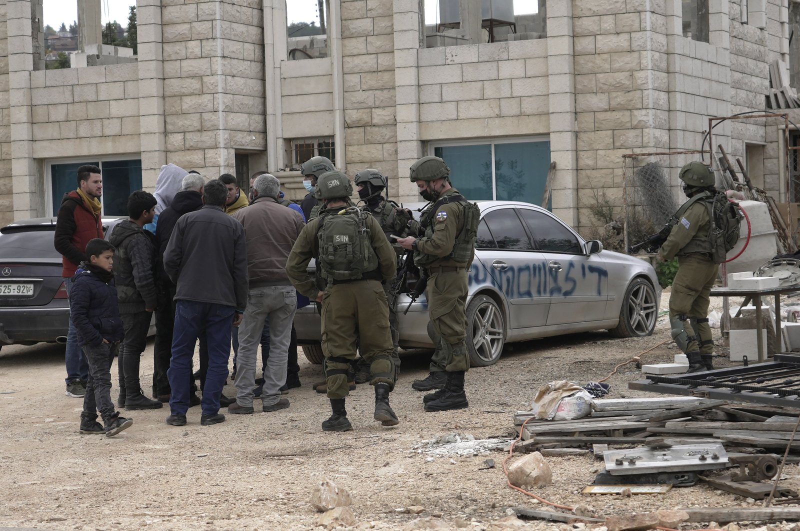 Israeli soldiers stand next to cars that Palestinians said Jewish settlers had vandalized, slashed the tires and sprayed paint on them with the Jewish Star of David and Hebrew that reads, &quot;Stop administrative detentions,&quot; in the village of Qira near the West Bank town of Salfit, Jan 23, 2022. (AP Photo)