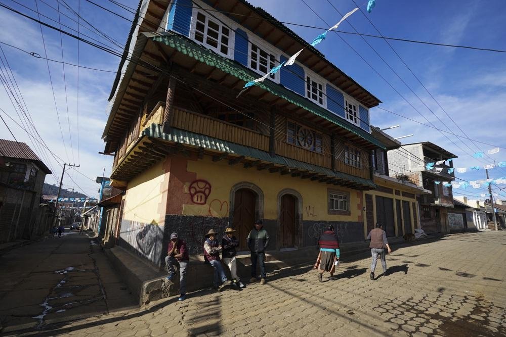 Residents gather on a street corner next to a home built with money earned in the United States, in the Puerpecha Indigenous community of Comachuen, Michoacan state, Mexico, Jan. 19, 2022. (AP Photo)
