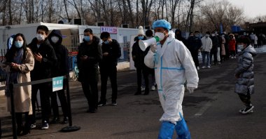 A staff member in a protective suit instructs people who are lining up for a throat swab test at a temporary COVID-19 testing center, Beijing, China, Jan. 26, 2022. (Reuters Photo)
