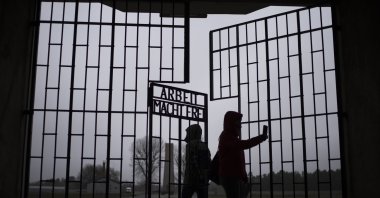People take photos as they enter the Sachsenhausen Nazi death camp through the gate with the phrase "Arbeit macht frei" (work sets you free), in Oranienburg, about 30 kilometers (18 miles) north of Berlin, Germany, Tuesday, Jan. 25, 2022. (AP Photo)