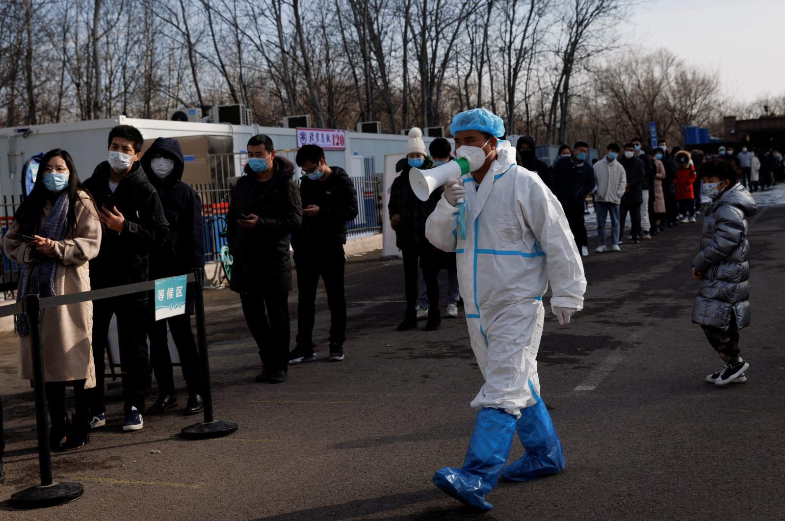 A staff member in a protective suit instructs people who are lining up for a throat swab test at a temporary COVID-19 testing center, Beijing, China, Jan. 26, 2022. (Reuters Photo)