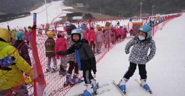School children play near a long line up to the bunny slope at a ski resort, in Yanqing, China, Dec. 23, 2021. (AP Photo)