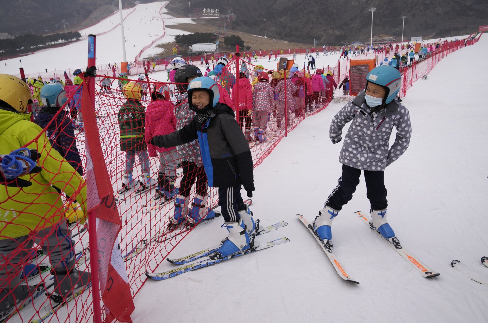 School children play near a long line up to the bunny slope at a ski resort, in Yanqing, China, Dec. 23, 2021. (AP Photo)