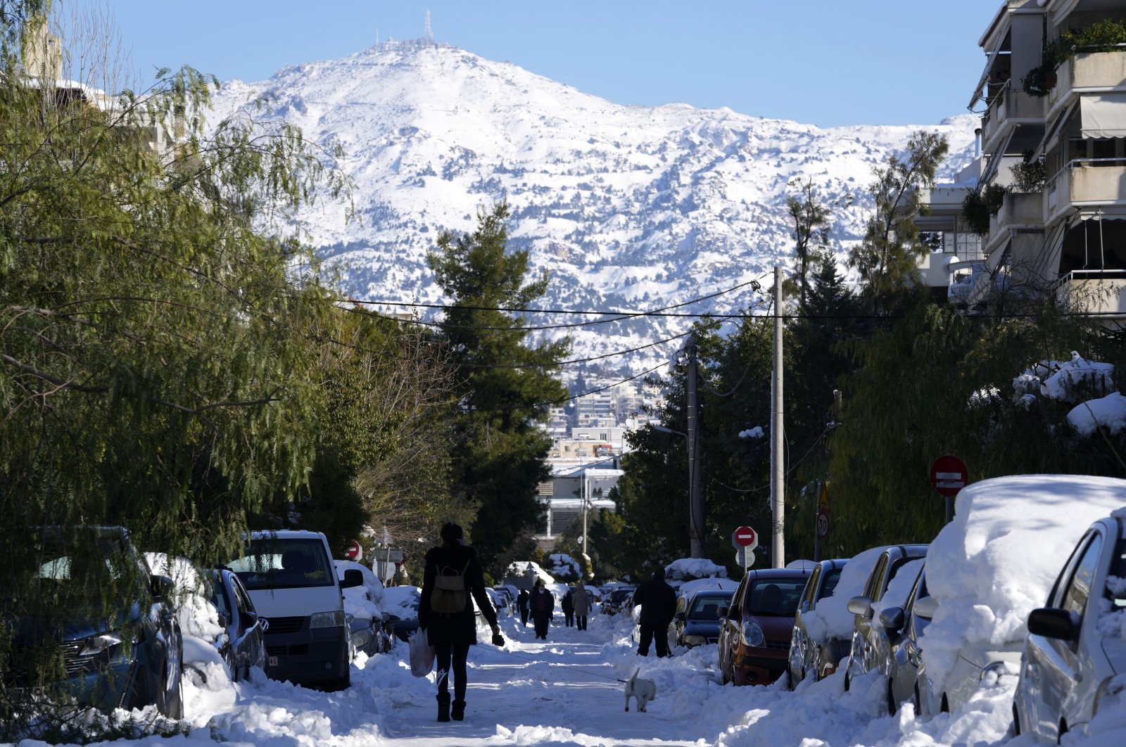 People walk on a frozen road after a snowstorm as Penteli mountain is seen in the background, in northern Athens, Greece, Jan. 26, 2022. (AP Photo)
