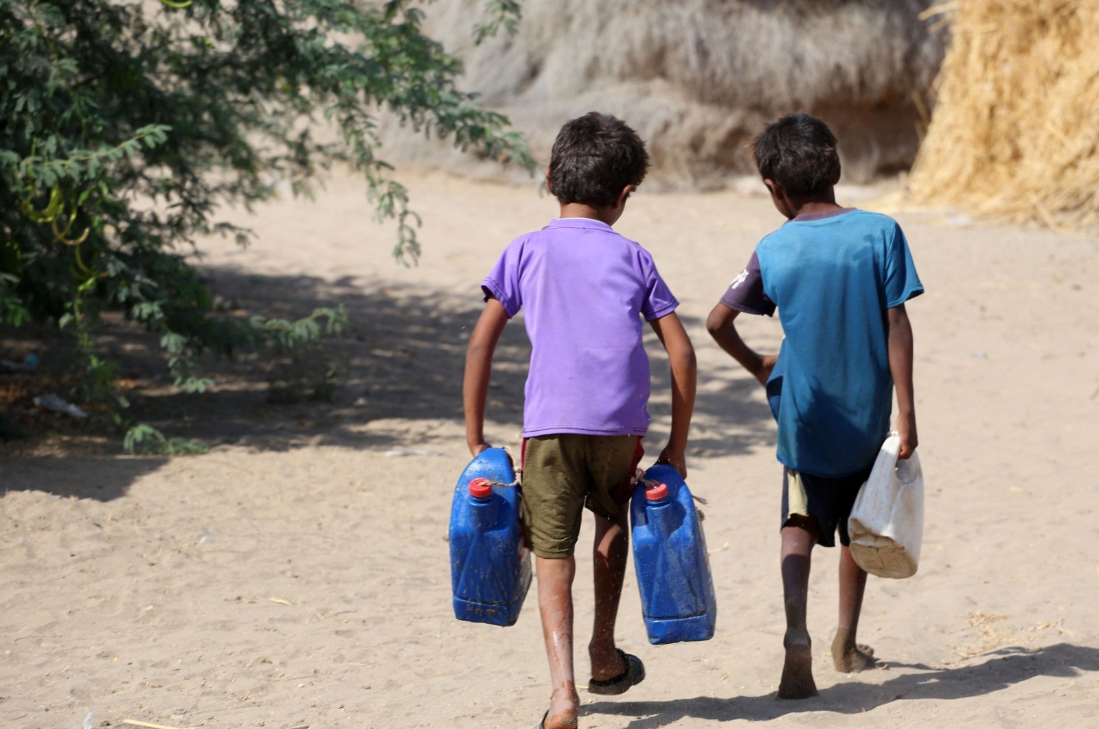 Yemeni children carry jerrycans at a makeshift camp for people who fled fighting between Huthi rebels and the Saudi-backed government forces, in the village of Hays near the conflict zone in Yemen&#039;s western province of Hodeida, on Jan. 28, 2022. (AFP Photo)