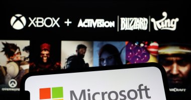 The Microsoft logo is seen on a phone screen in front of the official poster announcing the acquisition of Activision Blizzard, Jan. 18, 2022. (AA File Photo)