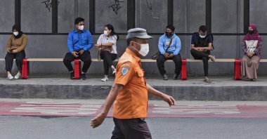 People wearing masks to help curb the spread of the COVID-19 outbreak sit at a bus stop in Medan, North Sumatra, Indonesia, Jan. 29, 2022. (AP Photo)
