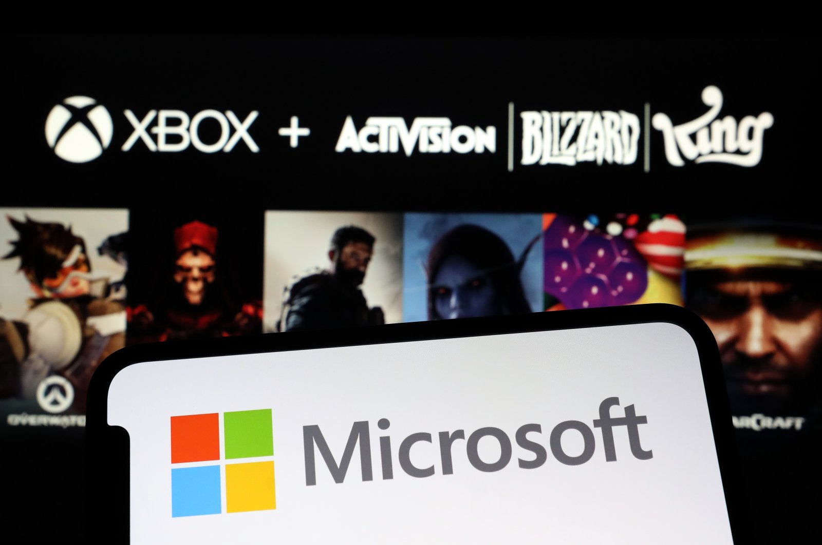 The Microsoft logo is seen on a phone screen in front of the official poster announcing the acquisition of Activision Blizzard, Jan. 18, 2022. (AA File Photo)