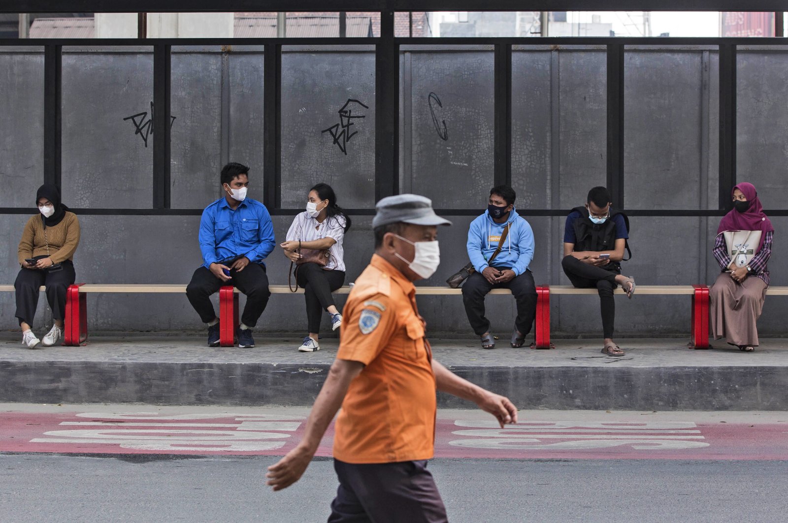 People wearing masks to help curb the spread of the COVID-19 outbreak sit at a bus stop in Medan, North Sumatra, Indonesia, Jan. 29, 2022. (AP Photo)