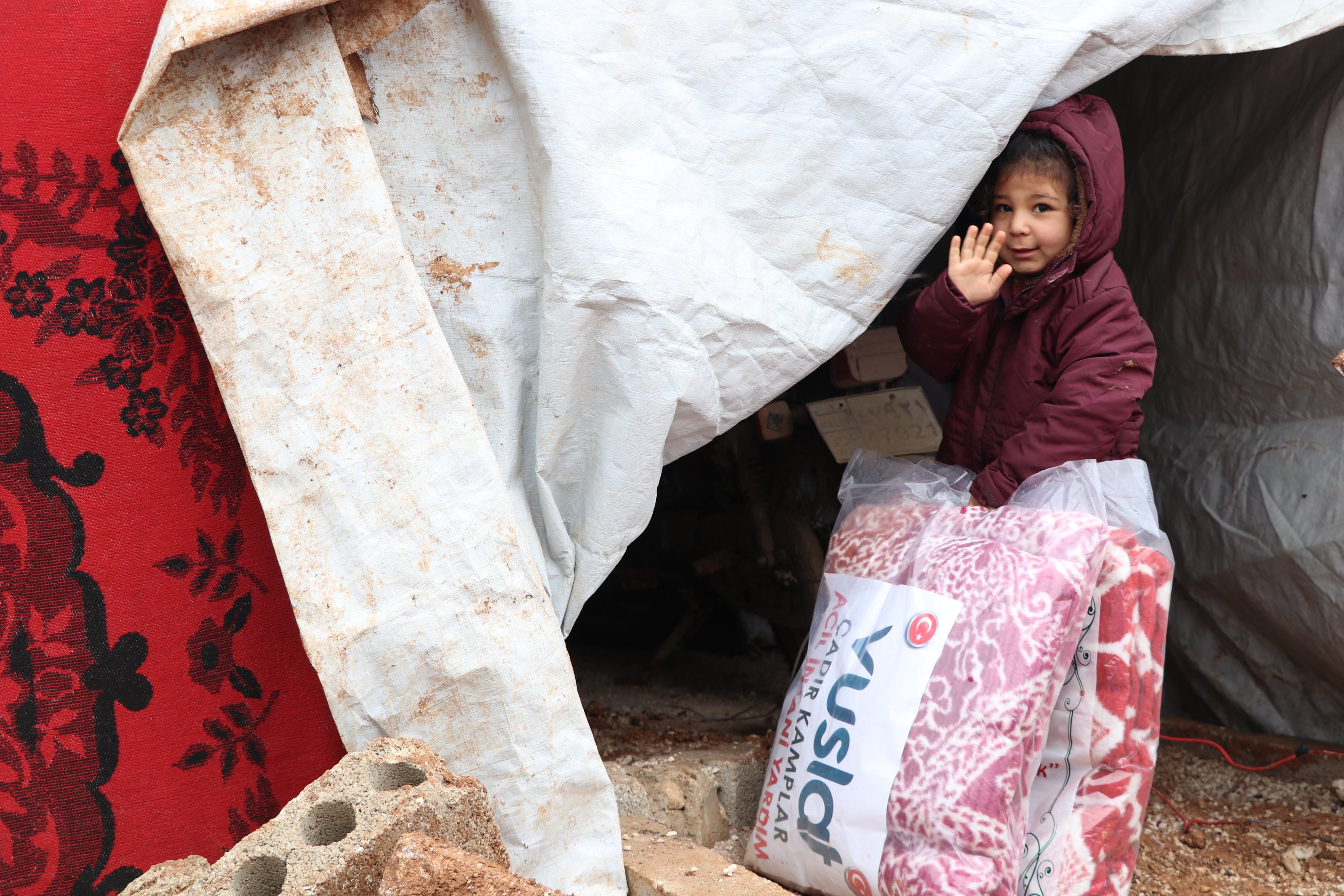A little girl waves as she enters her tent with the aid kit, Idlib, northwestern Syria, Feb. 1, 2022. (AA Photo)