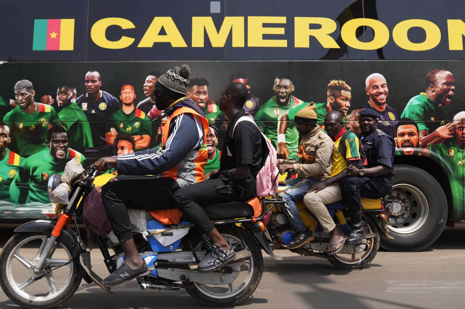 People on motorcycles ride past a bus painted in traditional colors of the Cameroon national team, Yaounde, Cameroon, Monday, Jan. 31, 2022. (AP Photo)