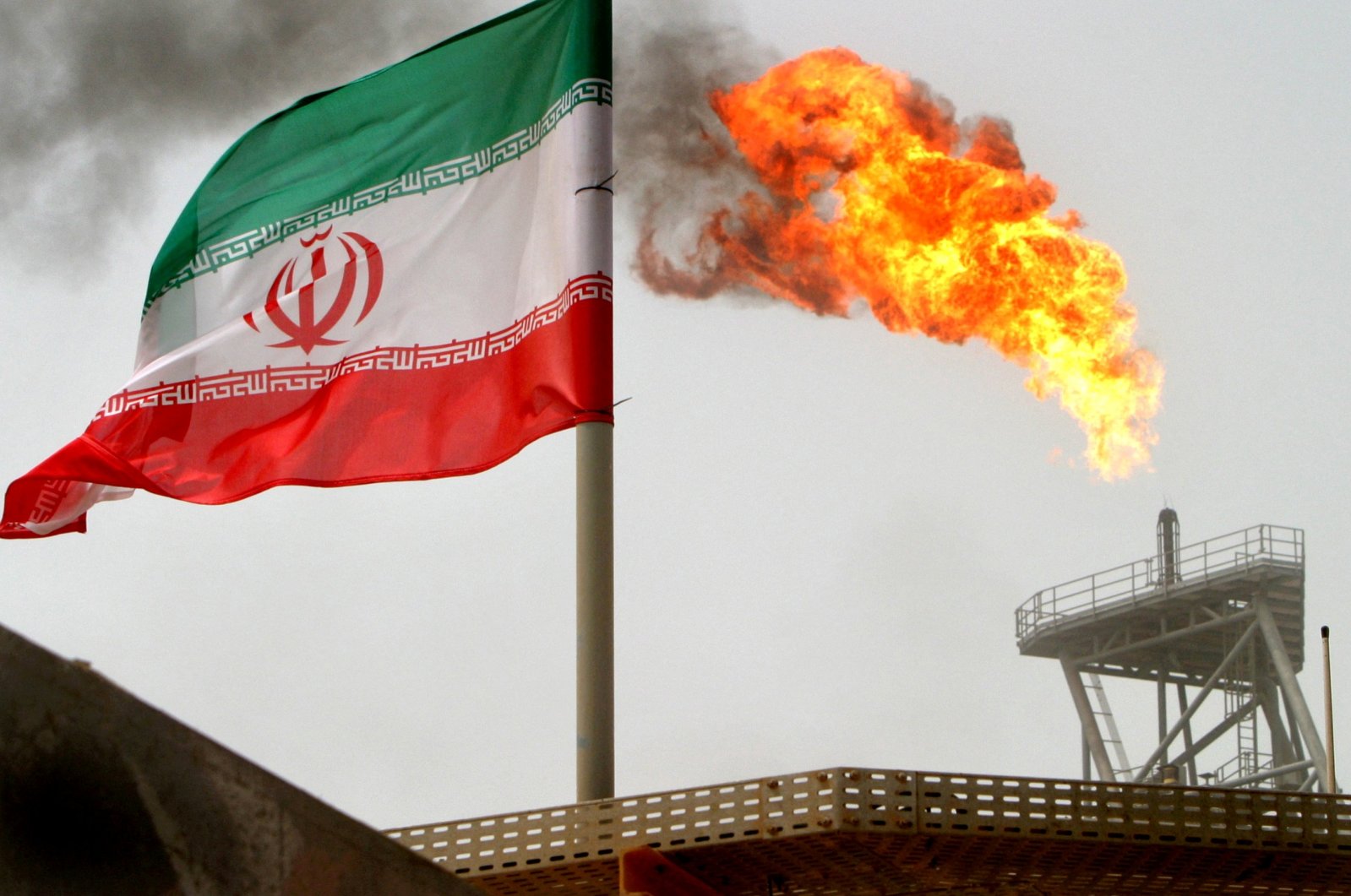 A gas flare on an oil production platform is seen alongside an Iranian flag in the Gulf, July 25, 2005. (Reuters Photo)