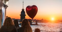 A red heart-shaped balloon flies over the heads of girls enjoying an amazing view of the Maiden's Tower at sunset, Istanbul, Turkey. (Shutterstock Photo)