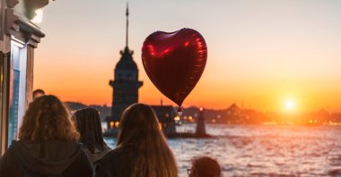 A red heart-shaped balloon flies over the heads of girls enjoying an amazing view of the Maiden&#039;s Tower at sunset, Istanbul, Turkey. (Shutterstock Photo)