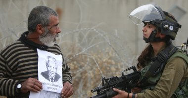 A Palestinian demonstrator holds portraits of late South African leader Nelson Mandela and late Palestinian leader Yasser Arafat as he stands in front of an Israeli soldier during a weekly demonstration against Israel's separation barrier, in the West Bank village of Bilin, near Ramallah, Dec. 6, 2013. (AP Photo)
