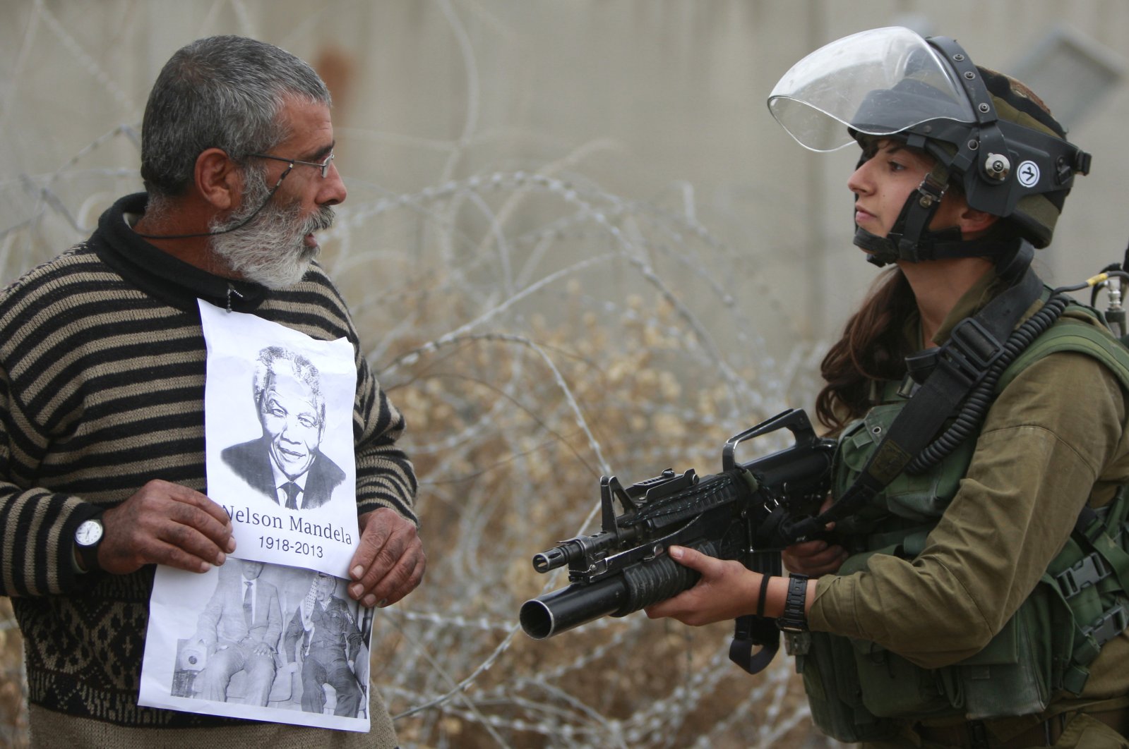 A Palestinian demonstrator holds portraits of late South African leader Nelson Mandela and late Palestinian leader Yasser Arafat as he stands in front of an Israeli soldier during a weekly demonstration against Israel&#039;s separation barrier, in the West Bank village of Bilin, near Ramallah, Dec. 6, 2013. (AP Photo)
