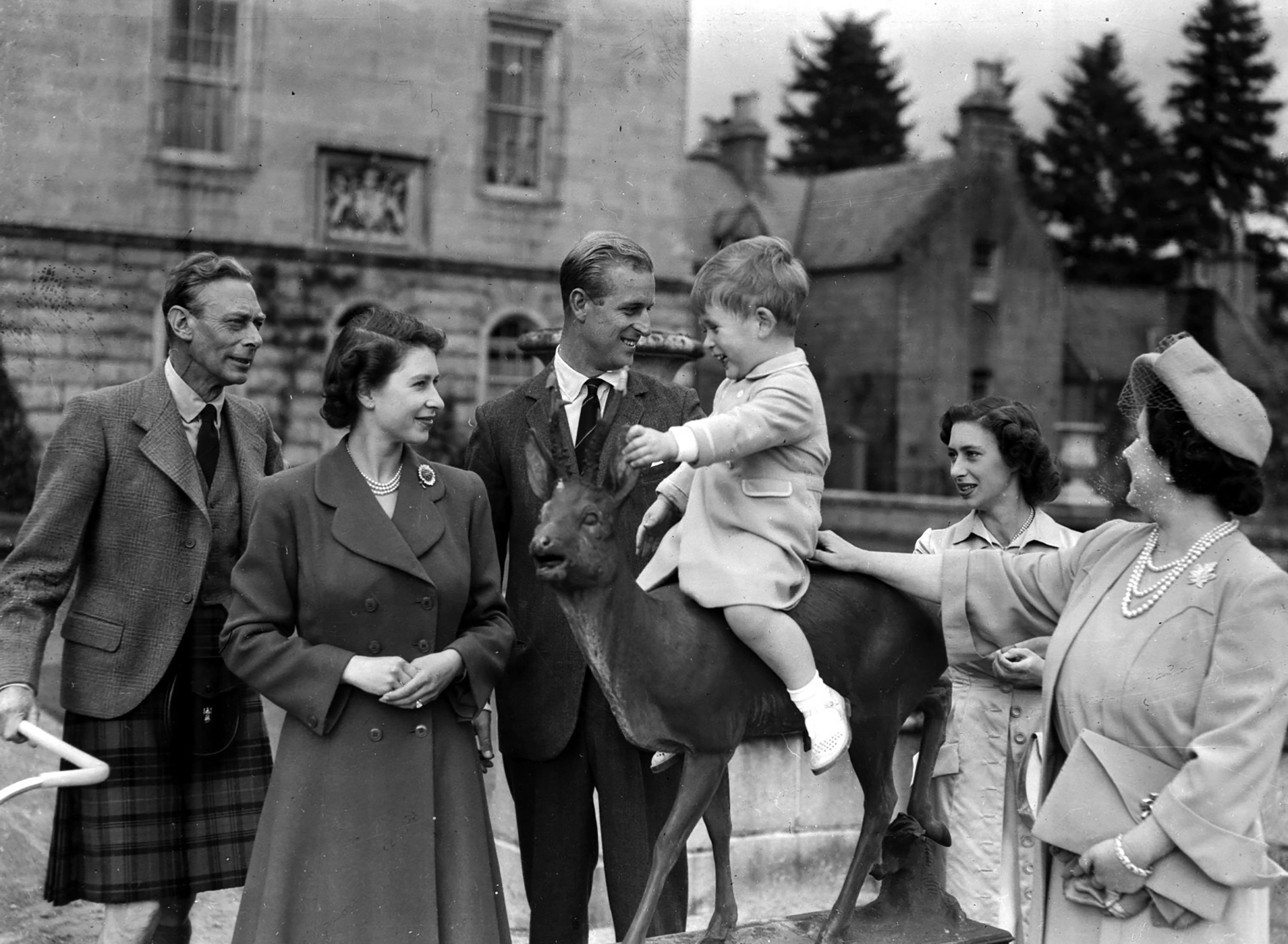 Prince Charles (C-R), watched by King George VI (L), Princess Elizabeth (C-L), Prince Philip (C), Princess Margaret and Queen Elizabeth (R), sits on a sculpture of a deer in the grounds of Balmoral Castle, Scotland, Aug. 1951. (AP Photo)