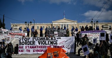 Protesters hold signs and banners as they stand next to a life raft during a demonstration in central Athens, Greece, on Feb. 6, 2022. (AFP Photo)