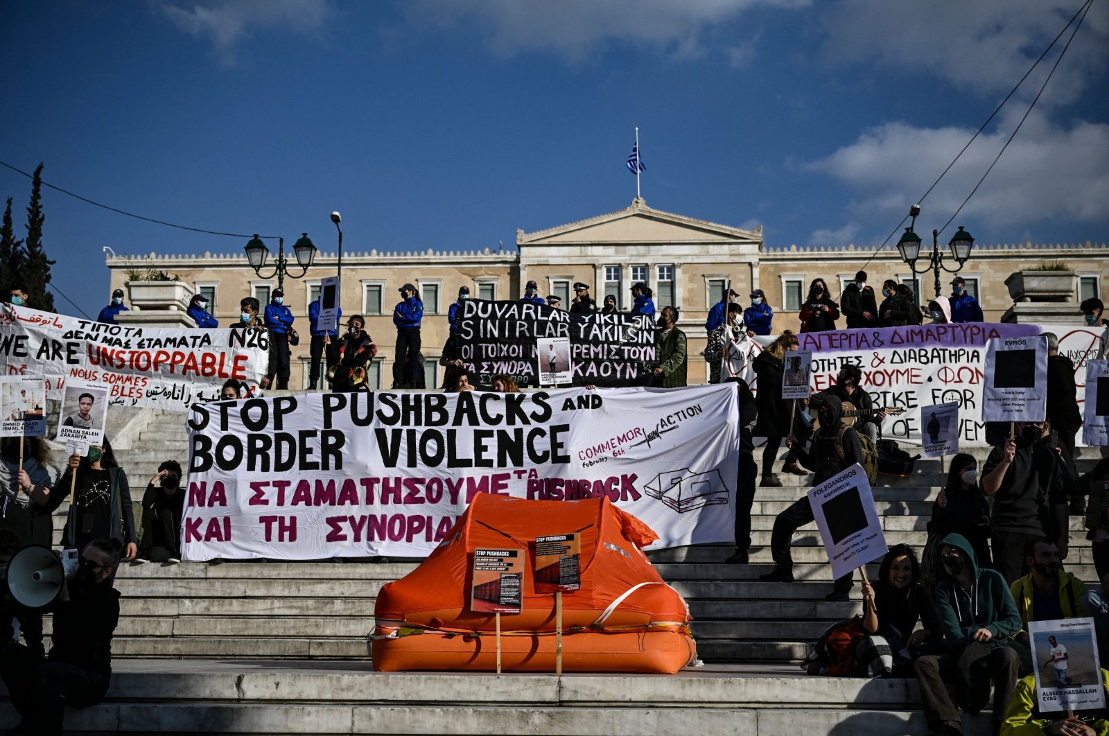 Protesters hold signs and banners as they stand next to a life raft during a demonstration in central Athens, Greece, on Feb. 6, 2022. (AFP Photo)