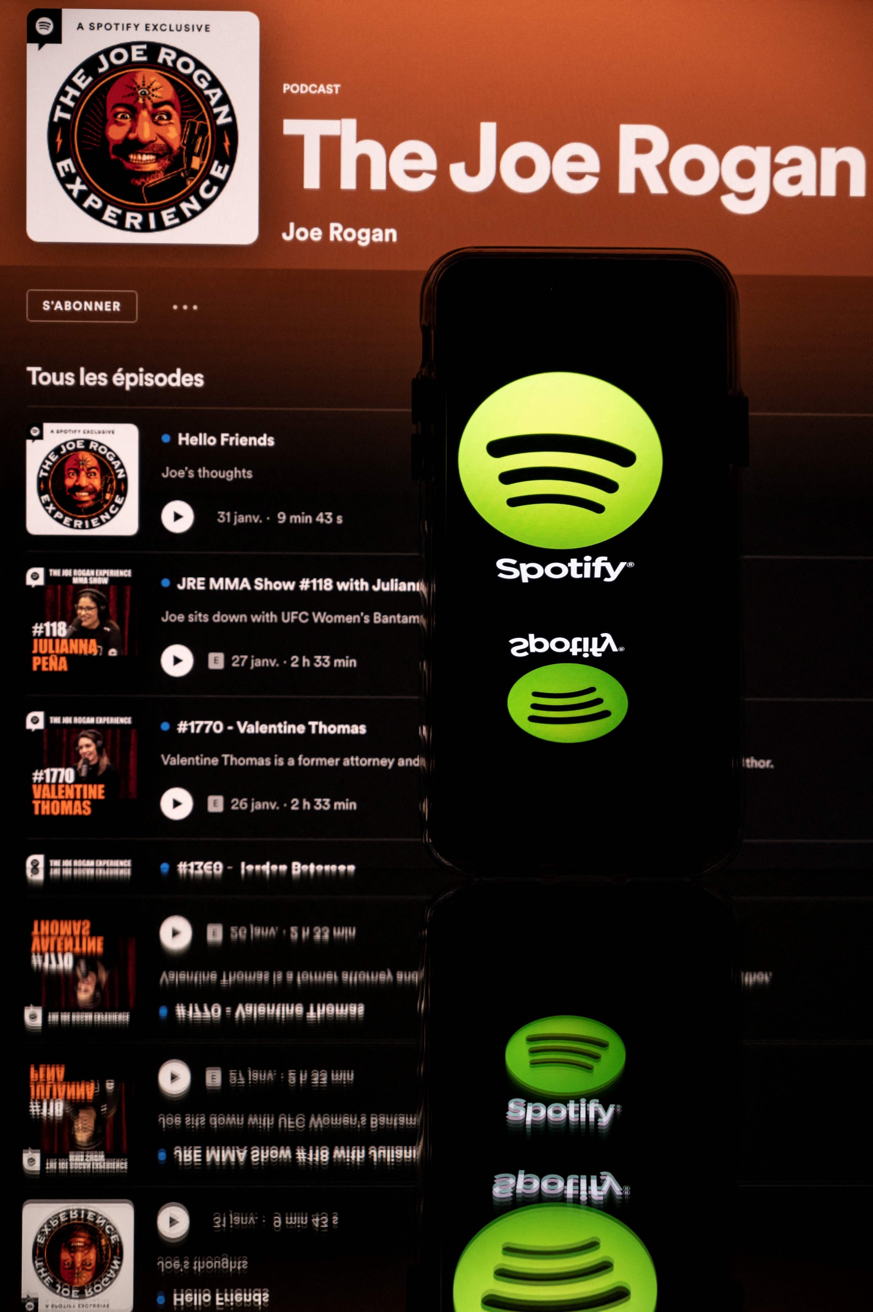 Foto tersebut menunjukkan layar yang menampilkan podcast Joe Rogan dan smartphone dengan logo Spotify, Toulouse, barat daya Prancis, 31 Januari 2022. (AFP Photo)