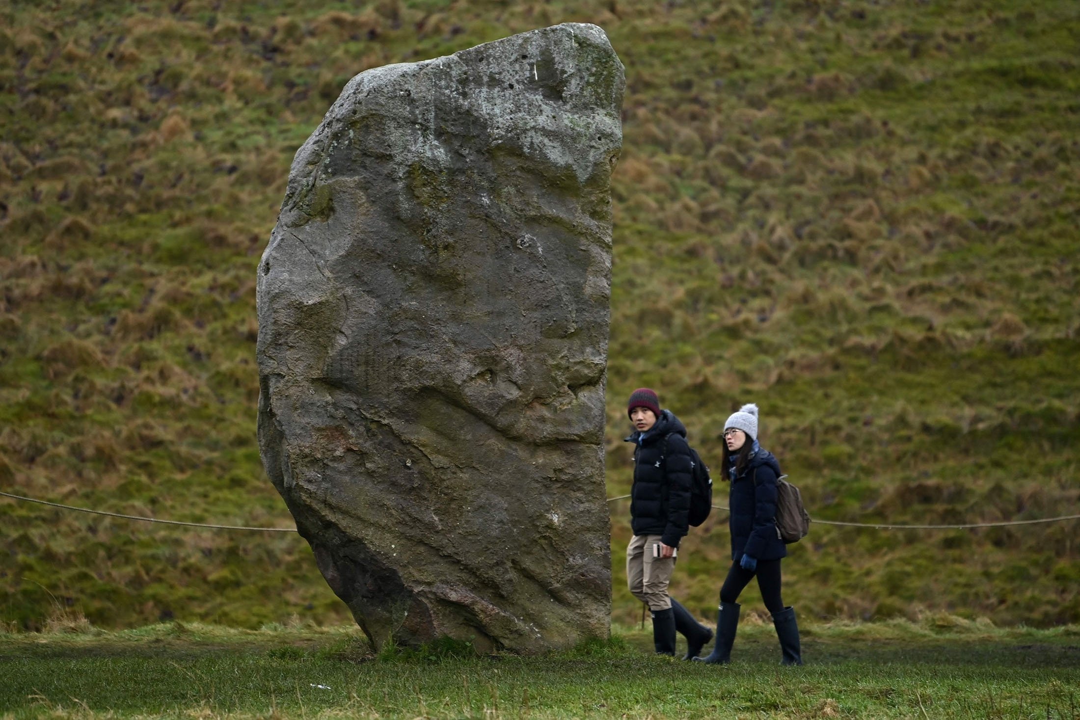 People walk past a stone that fomrms part of the Stone Circle in Avebury, southern England, Jan. 19, 2022. (AFP Photo)